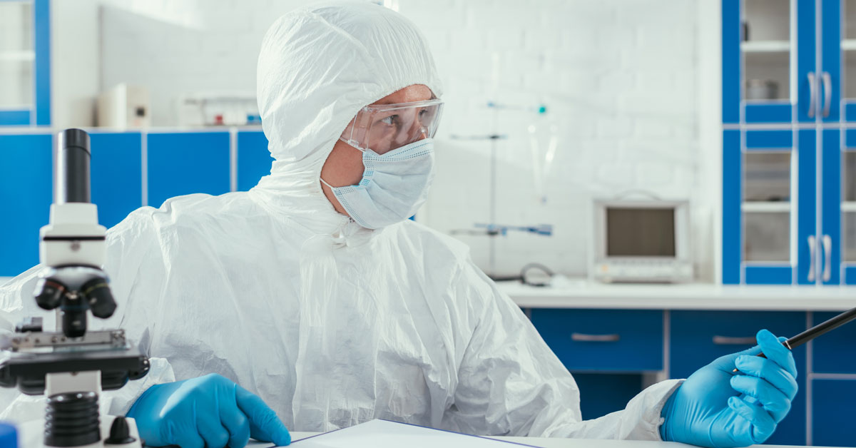 Biochemist in hazmat suit sitting near microscope